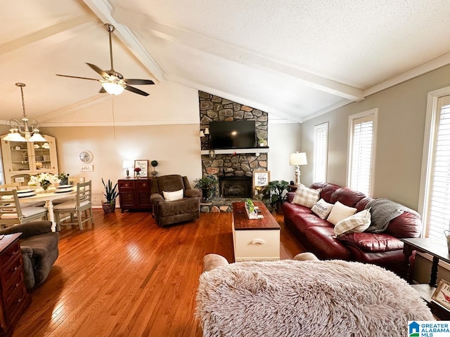 living room featuring lofted ceiling with beams, ceiling fan, a stone fireplace, a textured ceiling, and wood finished floors