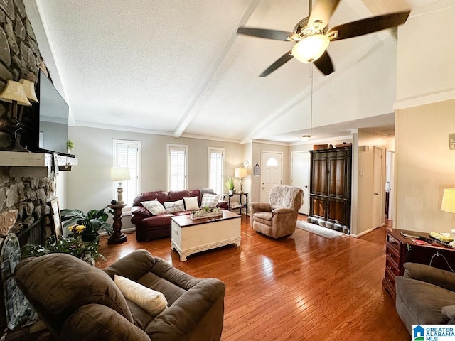 living room with a textured ceiling, ceiling fan, a stone fireplace, beamed ceiling, and wood-type flooring