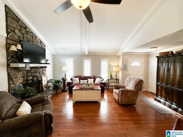 living room featuring dark wood-type flooring, a stone fireplace, ceiling fan, and lofted ceiling with beams