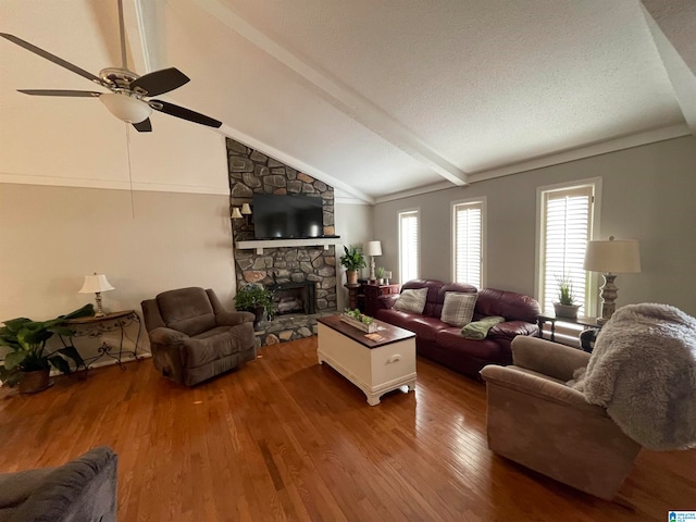 living area with a ceiling fan, lofted ceiling with beams, hardwood / wood-style floors, a textured ceiling, and a fireplace