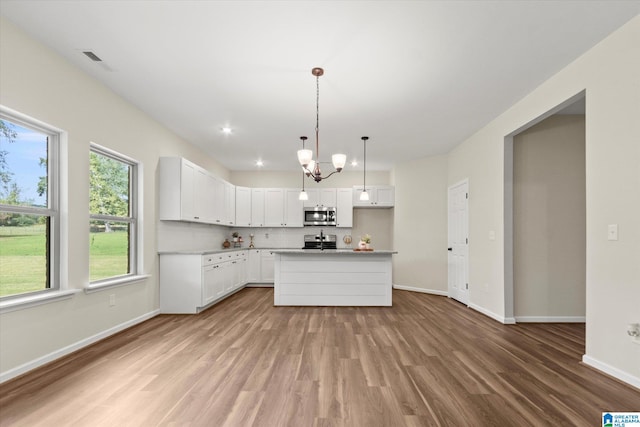 kitchen featuring white cabinets, stainless steel appliances, pendant lighting, light hardwood / wood-style floors, and a center island