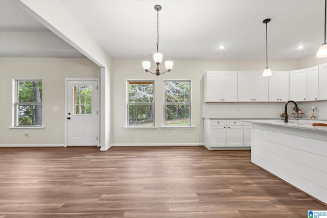 kitchen featuring light stone counters, hardwood / wood-style floors, white cabinetry, and hanging light fixtures