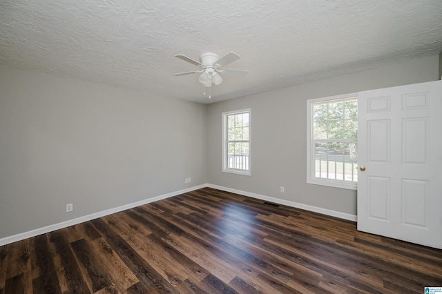 empty room featuring a textured ceiling, a healthy amount of sunlight, and dark hardwood / wood-style flooring