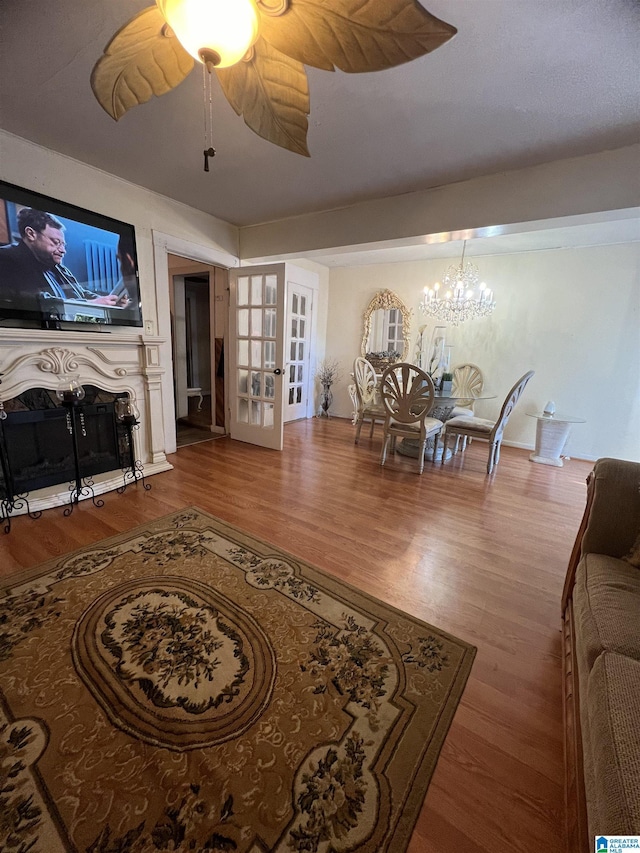 living area with wood finished floors, a chandelier, french doors, a glass covered fireplace, and a ceiling fan