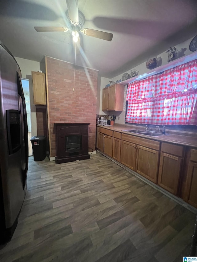 kitchen with stainless steel refrigerator with ice dispenser, a sink, ceiling fan, dark wood-style floors, and a brick fireplace