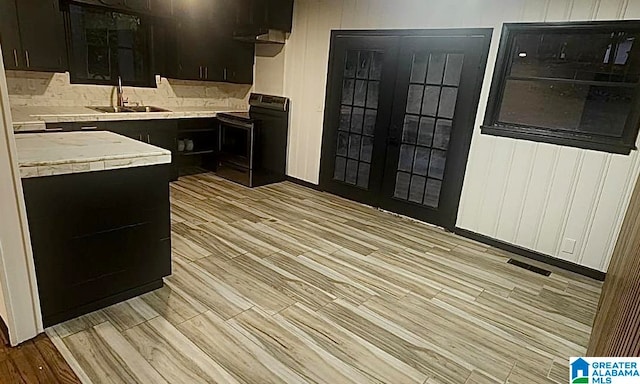 kitchen with light hardwood / wood-style flooring, black electric range oven, sink, and wooden walls