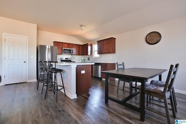 kitchen featuring dark wood-type flooring, a center island, a kitchen bar, vaulted ceiling, and appliances with stainless steel finishes