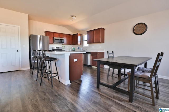 kitchen featuring lofted ceiling, a breakfast bar area, appliances with stainless steel finishes, dark hardwood / wood-style flooring, and a center island