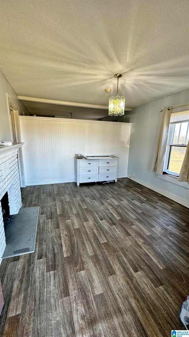 unfurnished living room with a textured ceiling, a chandelier, dark wood-type flooring, and a brick fireplace