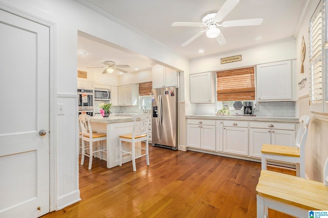 kitchen featuring decorative backsplash, white cabinets, a kitchen bar, light wood-type flooring, and stainless steel appliances