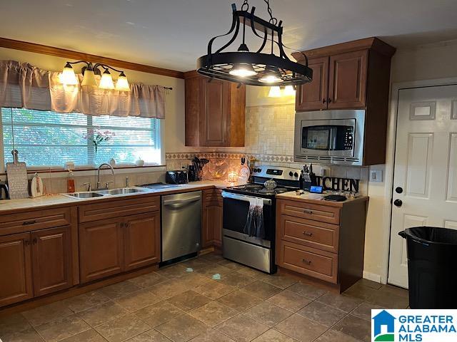 kitchen with hanging light fixtures, backsplash, appliances with stainless steel finishes, crown molding, and sink