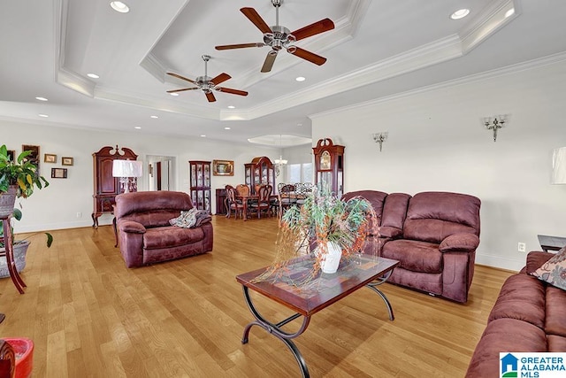 living room featuring ceiling fan, light wood-type flooring, crown molding, and a tray ceiling