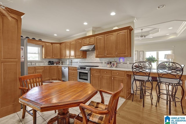 kitchen with kitchen peninsula, a wealth of natural light, stainless steel appliances, and ornamental molding