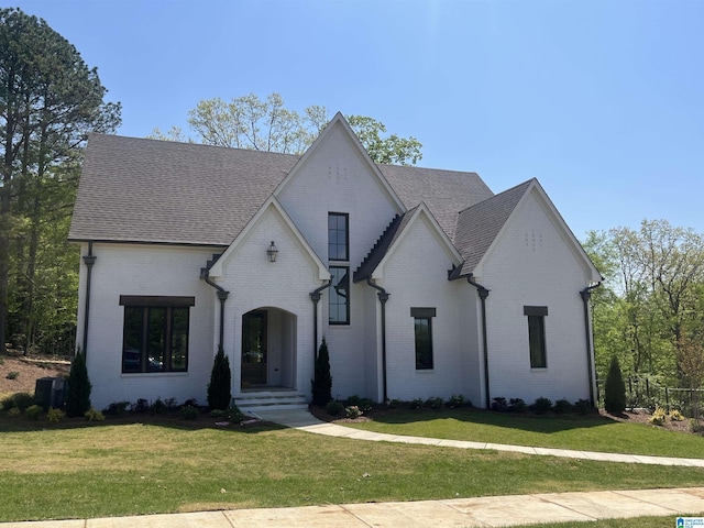 view of front of property featuring roof with shingles, central AC unit, a front yard, and brick siding
