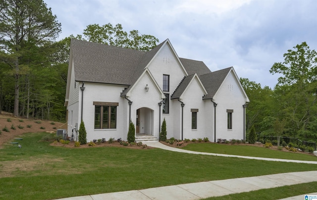 french country home with central AC unit, roof with shingles, and a front yard