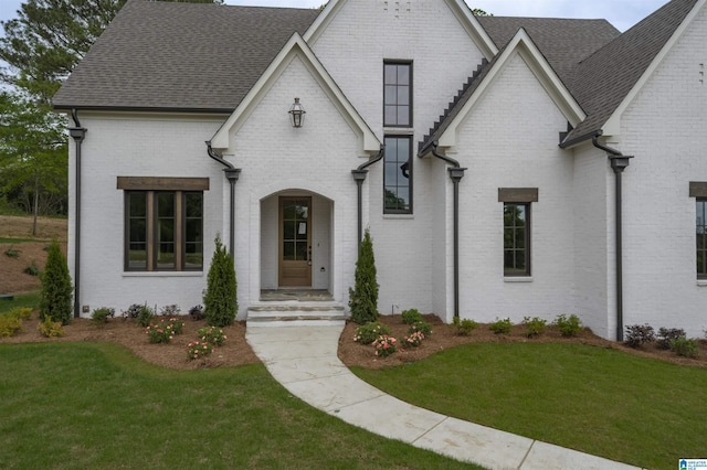 view of front of home featuring brick siding, roof with shingles, and a front yard