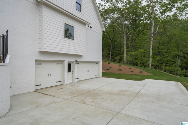 view of side of home featuring an attached garage, a view of trees, brick siding, and concrete driveway