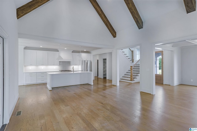 unfurnished living room featuring visible vents, beamed ceiling, stairway, high vaulted ceiling, and light wood-type flooring