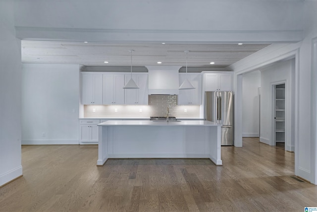 kitchen featuring a sink, light countertops, a kitchen island with sink, high end refrigerator, and custom range hood