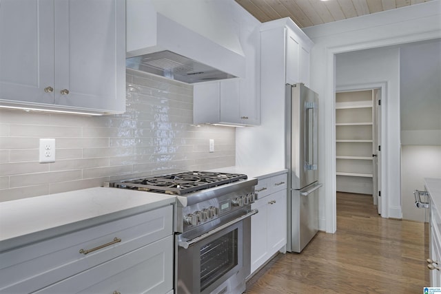 kitchen with decorative backsplash, appliances with stainless steel finishes, wood finished floors, white cabinets, and custom exhaust hood