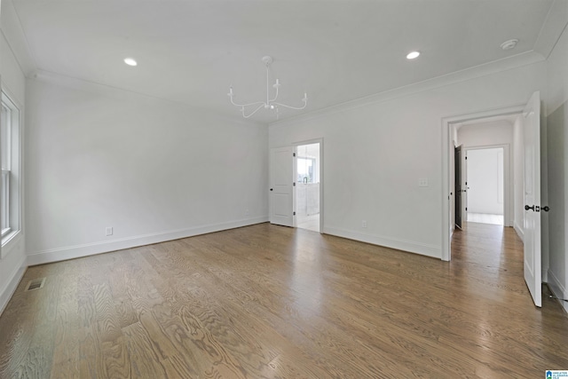 empty room featuring an inviting chandelier, ornamental molding, visible vents, wood finished floors, and baseboards