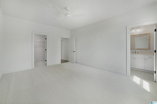 unfurnished bedroom with baseboards, ensuite bath, a spacious closet, and light carpet