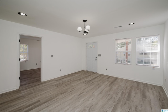 empty room with a wealth of natural light, a notable chandelier, and light wood-type flooring