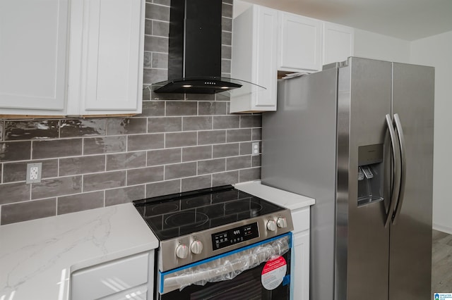 kitchen featuring wall chimney range hood, tasteful backsplash, appliances with stainless steel finishes, white cabinetry, and light stone counters