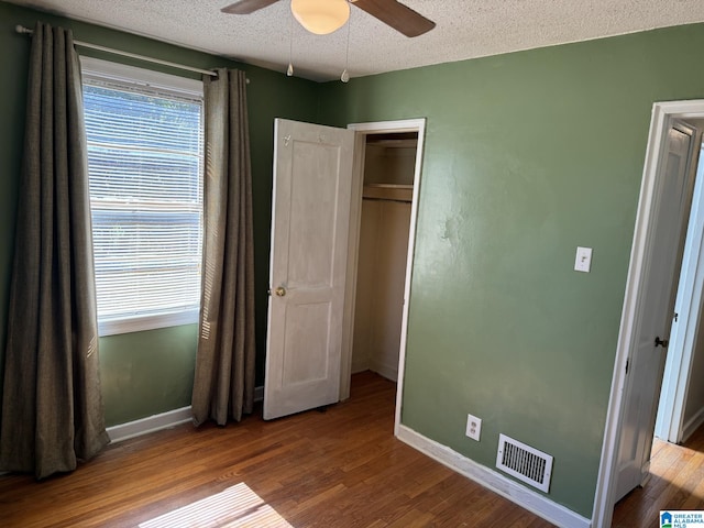 unfurnished bedroom featuring a closet, hardwood / wood-style floors, a textured ceiling, and ceiling fan