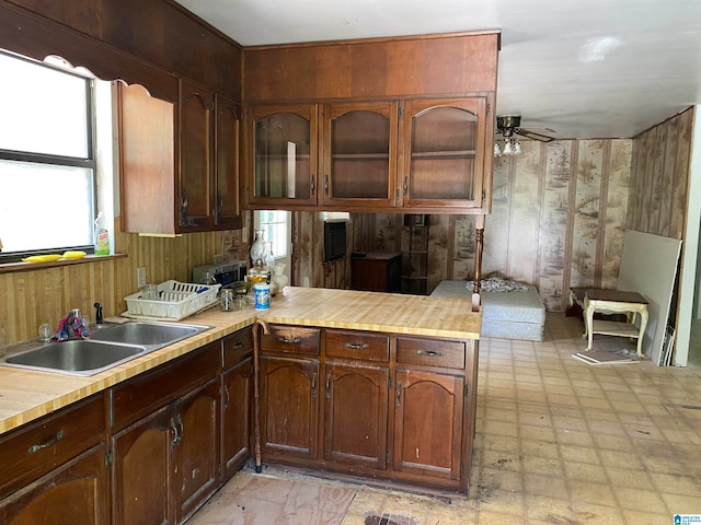 kitchen featuring kitchen peninsula, wood walls, sink, and ceiling fan