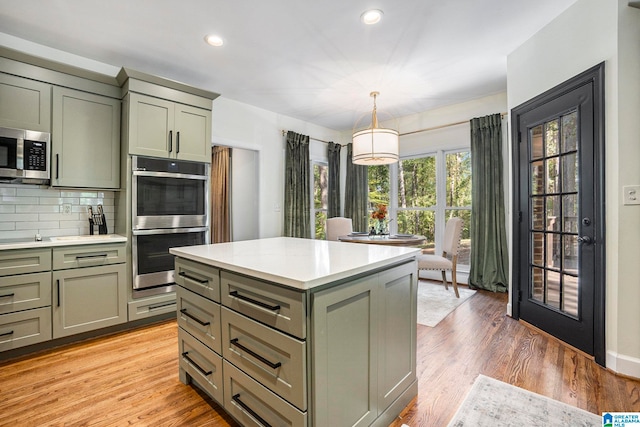 kitchen with appliances with stainless steel finishes, green cabinetry, backsplash, hanging light fixtures, and light hardwood / wood-style floors