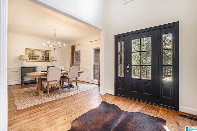 foyer entrance featuring an inviting chandelier, ornamental molding, and light wood-type flooring