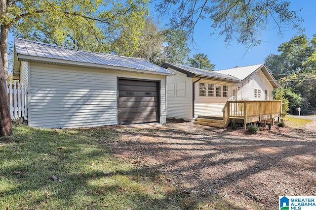 exterior space featuring a wooden deck, a garage, an outbuilding, and a lawn