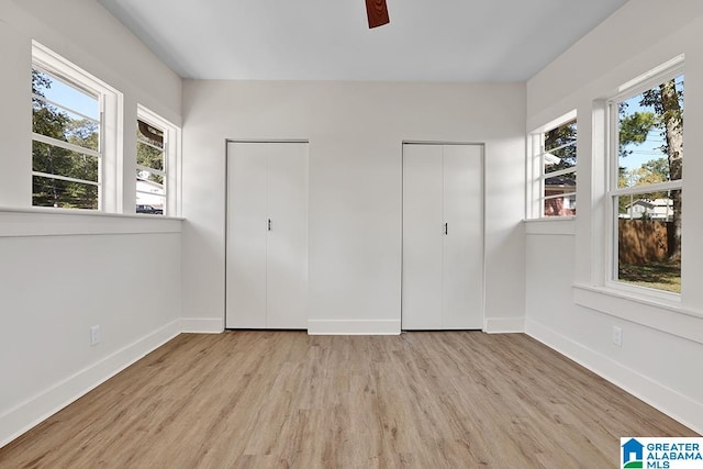 unfurnished bedroom featuring ceiling fan, light hardwood / wood-style flooring, and two closets