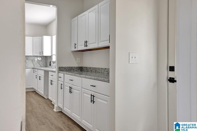 kitchen with white cabinets, light stone countertops, light wood-type flooring, and backsplash