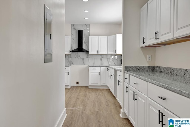 kitchen featuring wall chimney range hood, white cabinets, electric panel, light stone countertops, and light wood-type flooring