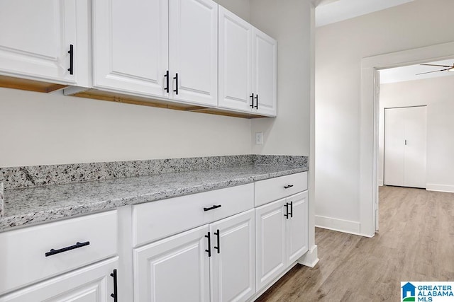 kitchen with light stone counters, white cabinetry, and light hardwood / wood-style flooring