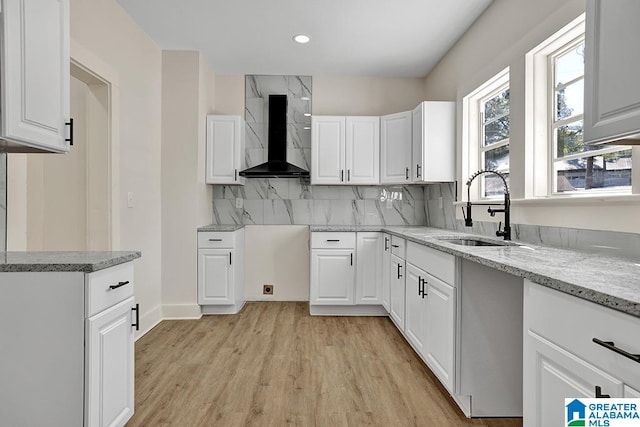 kitchen featuring light hardwood / wood-style floors, wall chimney exhaust hood, white cabinetry, and sink