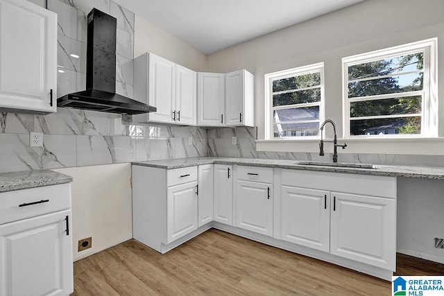 kitchen featuring white cabinets, decorative backsplash, light hardwood / wood-style floors, wall chimney exhaust hood, and sink