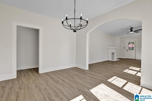 unfurnished dining area with hardwood / wood-style floors, a fireplace, and ceiling fan with notable chandelier