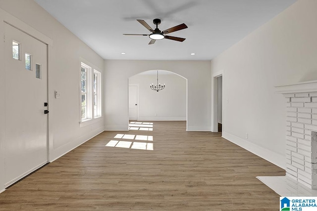 entryway with light hardwood / wood-style floors, a brick fireplace, and ceiling fan with notable chandelier