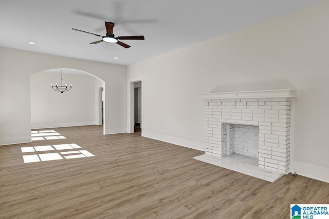 unfurnished living room with a fireplace, hardwood / wood-style flooring, and ceiling fan with notable chandelier