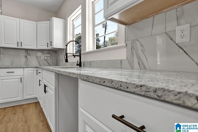 kitchen featuring white cabinetry, light stone counters, sink, and backsplash