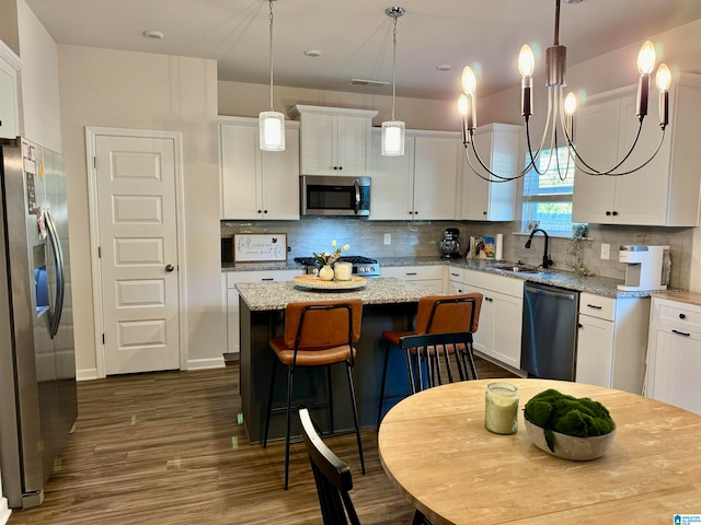 kitchen featuring hanging light fixtures, stainless steel appliances, a center island, white cabinetry, and light stone counters