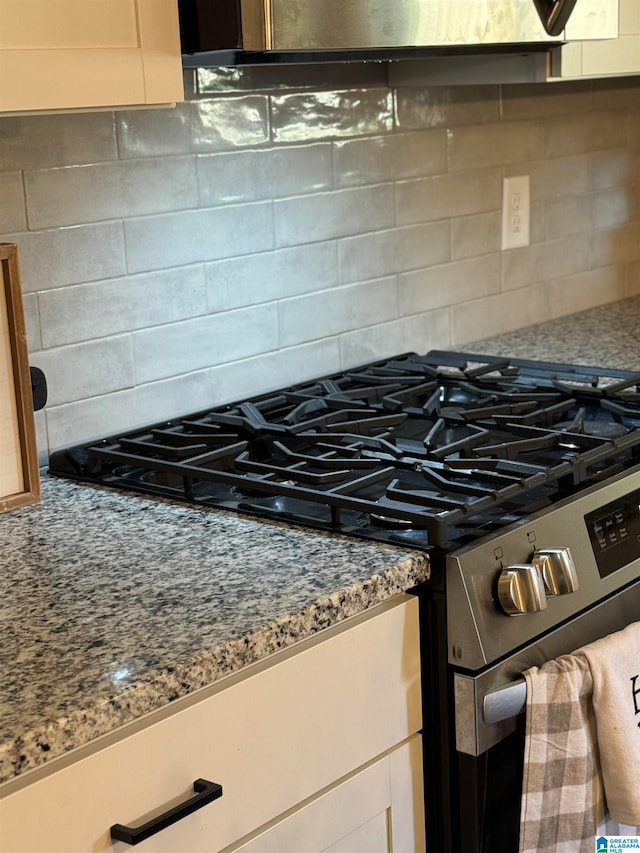 room details featuring white cabinetry, decorative backsplash, light stone counters, and high end stainless steel range