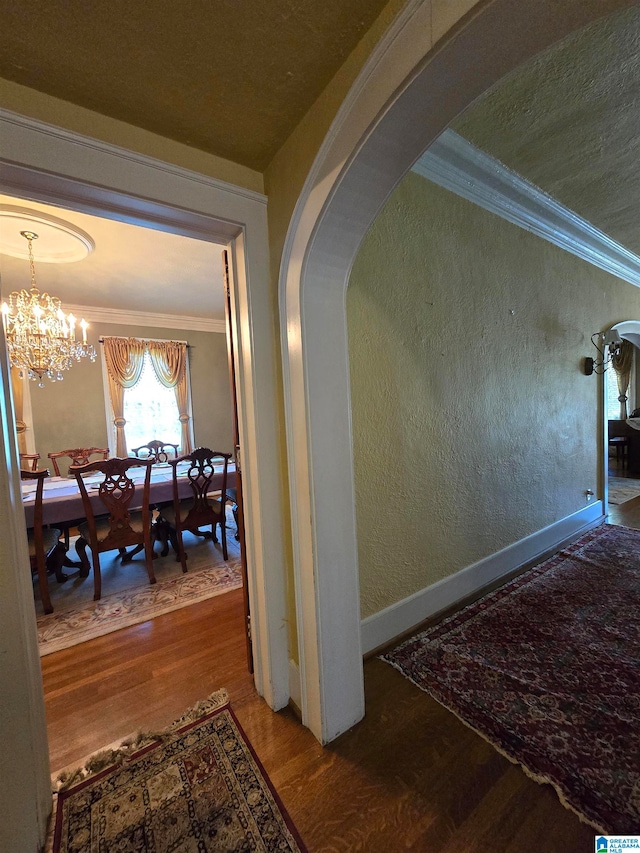 hall with a notable chandelier, wood-type flooring, and ornamental molding