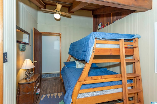 bedroom featuring ceiling fan, beam ceiling, wooden walls, and dark hardwood / wood-style floors