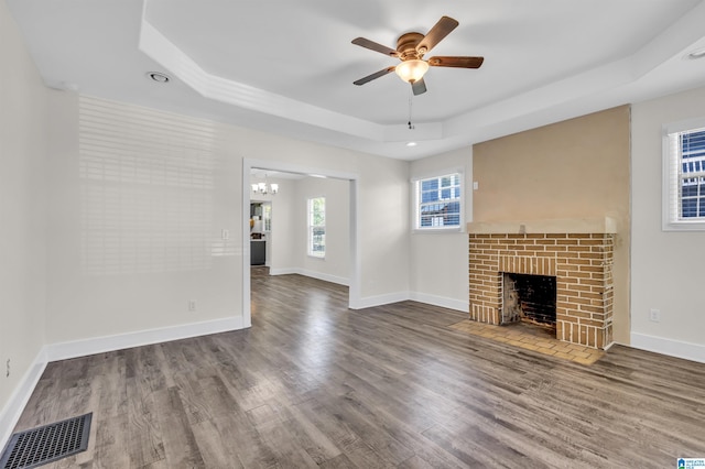 unfurnished living room featuring a fireplace, hardwood / wood-style flooring, ceiling fan with notable chandelier, and a raised ceiling