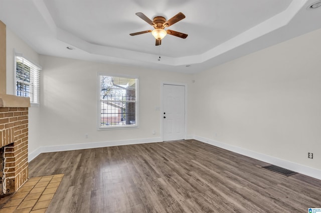 unfurnished living room featuring a wealth of natural light, a tray ceiling, and dark hardwood / wood-style flooring