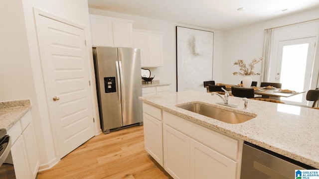 kitchen with stainless steel appliances, white cabinetry, sink, light stone countertops, and light hardwood / wood-style flooring